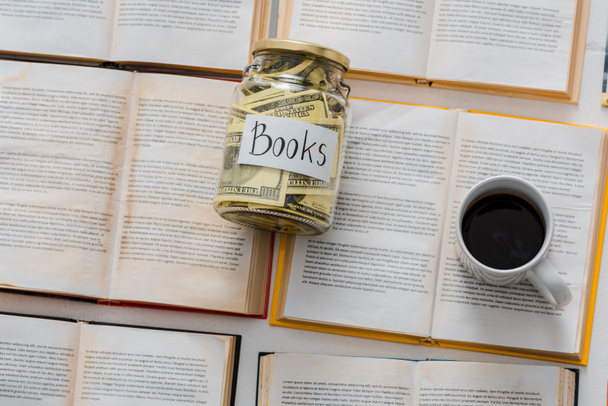 close up of money savings in jar with cup of coffee on open books  - 写真・画像