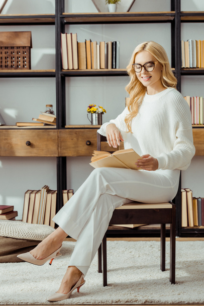 beautiful woman in glasses sitting and reading book in living room - Photo, Image
