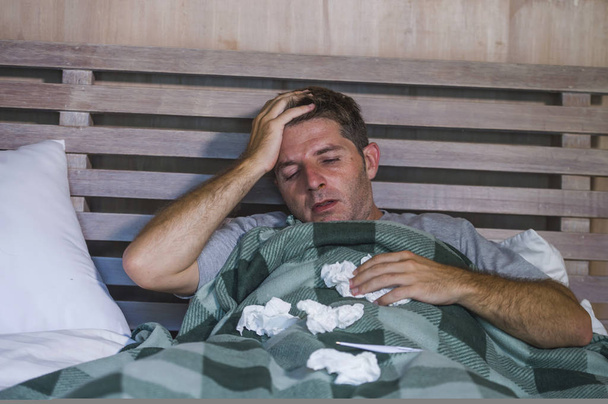 junger kranker und erschöpfter Mann im häuslichen Bett liegend, sich unwohl fühlend, Schnupfen und Grippe niesende Nase mit Geweben, die Viren und Kopfschmerzen im häuslichen Gesundheitswesen und Grippekonzept haben - Foto, Bild