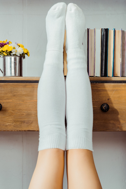Nahaufnahme von Frauenbeinen in weißen Socken auf Bücherregal - Foto, Bild