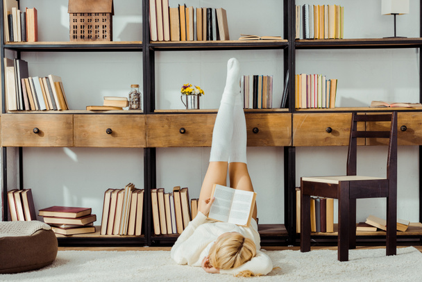mujer acostada en la alfombra y libro de lectura con piernas en rack
 - Foto, Imagen