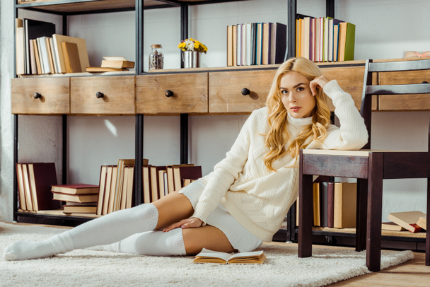 beautiful woman sitting on carpet with book in living room - Фото, изображение