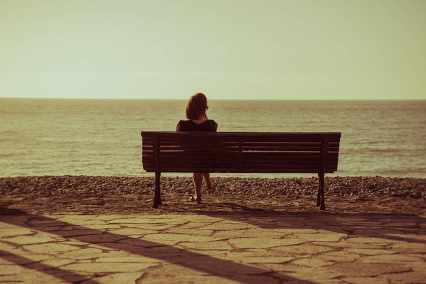 Silhouet van een jonge vrouw die alleen op de bank zit voor de oceaan - Foto, afbeelding