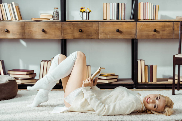 улыбающаяся красивая женщина лежит на ковре и читает книгу
 - Фото, изображение