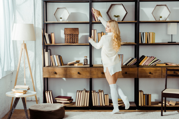 hermosa mujer adulta tomando libro de estante de madera
  - Foto, imagen