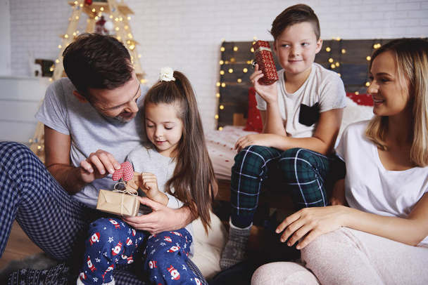 Szczęśliwa rodzina otwarcie Boże Narodzenie prezentuje w łóżku  - Zdjęcie, obraz