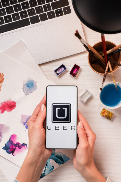 cropped view of designer holding smartphone with uber app on screen, flat lay - Fotó, kép