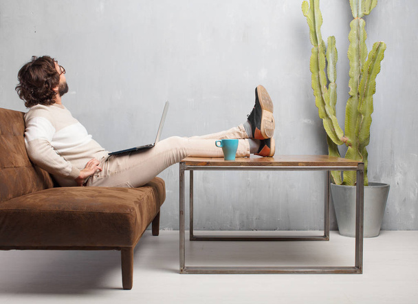 young bearded man sitting on a leather sofa in a vintage living room - Foto, afbeelding