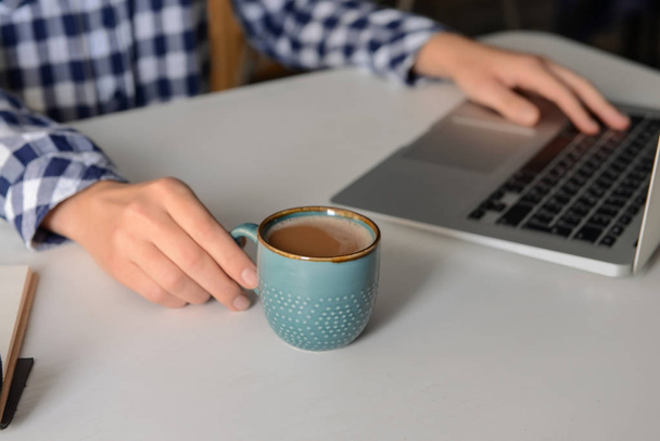 Mujer bebiendo café aromático mientras usa el ordenador portátil en la mesa
 - Foto, imagen