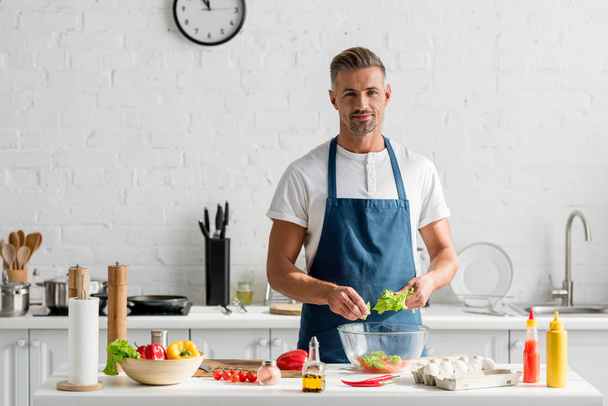 adult man in apron preparing salad at kitchen - Foto, immagini