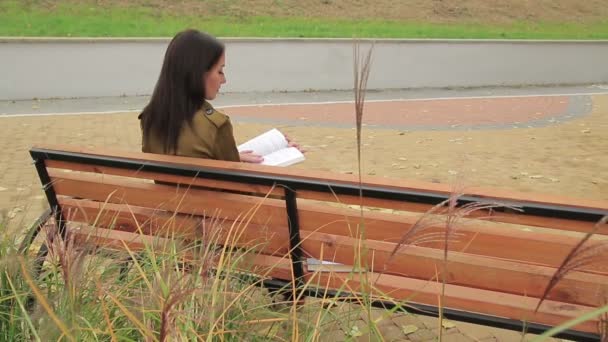 座っている女の子がベンチで本を返して表示 (1080、25 fps はフォア グラウンドでいくつかの高い草で読み取り) - 映像、動画