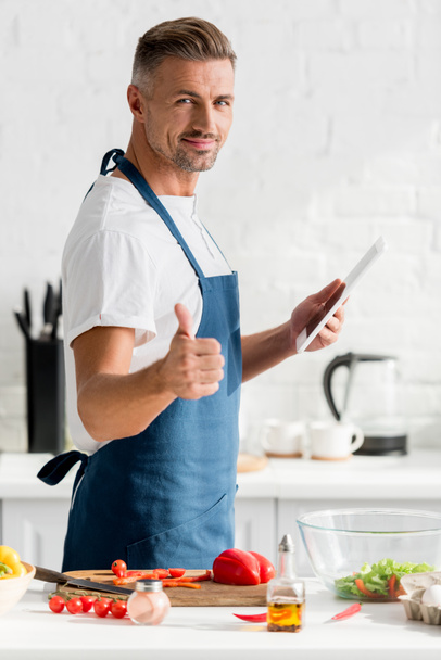 man with digital tablet showing thumbs up at kitchen - Foto, afbeelding