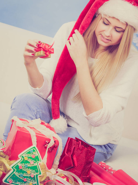 Holiday gifts, seasonal concept. Woman in Santa hat sitting on sofa preparing and packing christmas presents - Foto, afbeelding