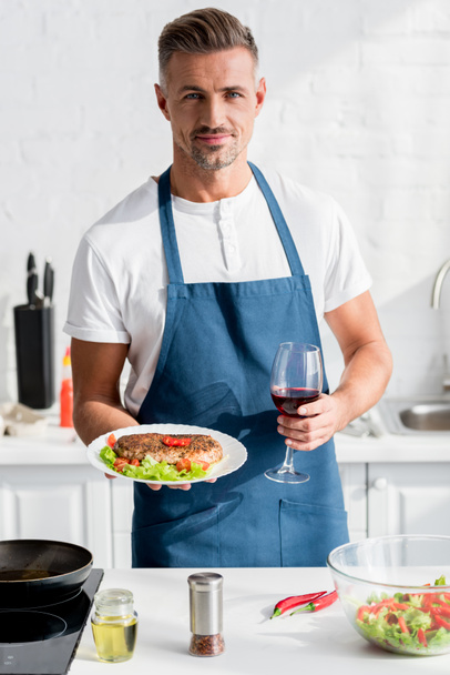 schöner Mann mit gekochtem Fleisch in der einen Hand und einem Glas Wein in der anderen - Foto, Bild