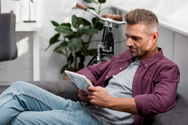 Homme assis sur le canapé et utilisant une tablette numérique - Photo, image