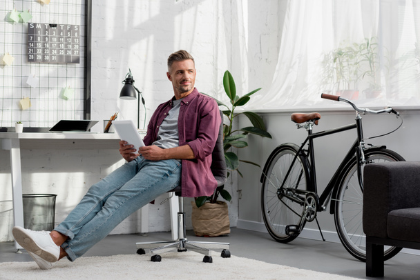 Lächelnder Mann auf Stuhl mit digitalem Tablet in der Hand - Foto, Bild