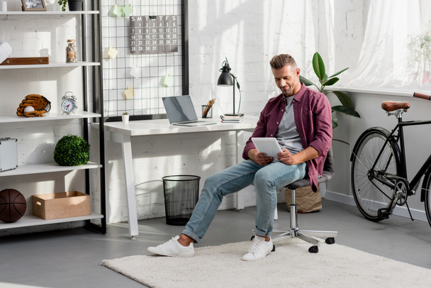 lächelnder Mann auf Stuhl sitzend und mit digitalem Tablet im Home Office - Foto, Bild