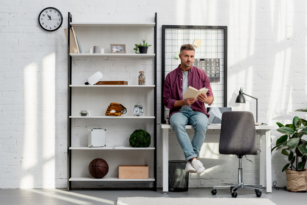man sitting on table and reading book at home office - Foto, Bild