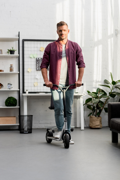 smiling man riding scooter at home office - Foto, Bild