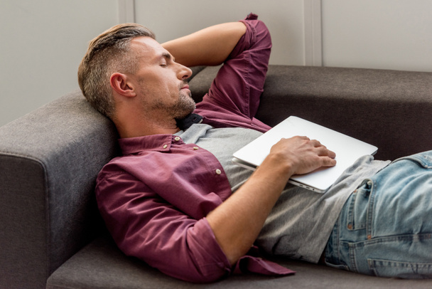 чоловік лежить на дивані з ноутбуком і спить в домашньому офісі
 - Фото, зображення