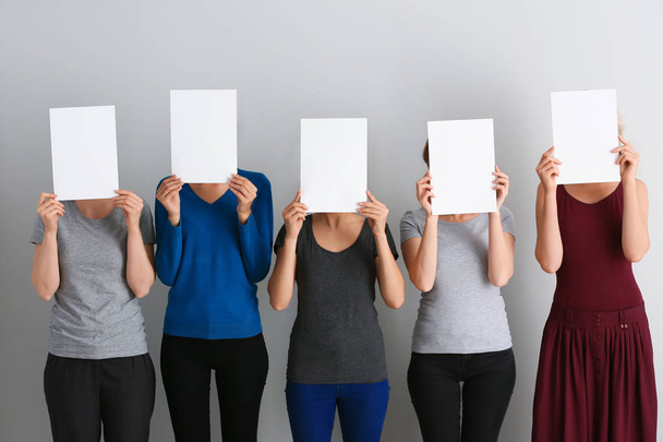 Young women hiding faces behind blank sheets of paper on light background - Photo, Image