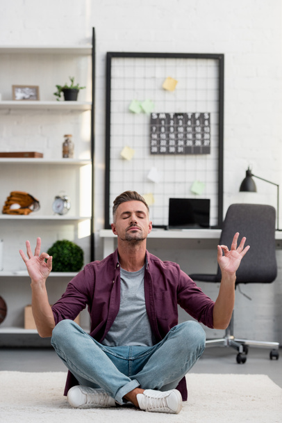 hombre sentado en el suelo y practicando yoga en casa oficina
 - Foto, imagen