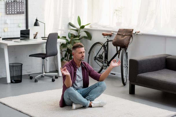 концентрированный мужчина, сидящий на полу и практикующий йогу в домашнем офисе
  - Фото, изображение