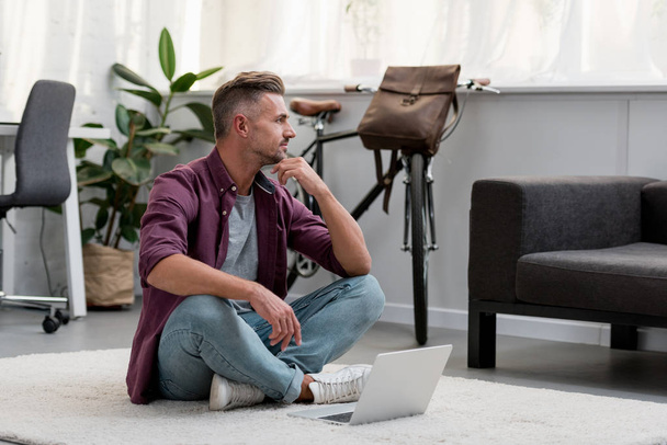 homem pensativo sentado no chão no escritório em casa com laptop
 - Foto, Imagem