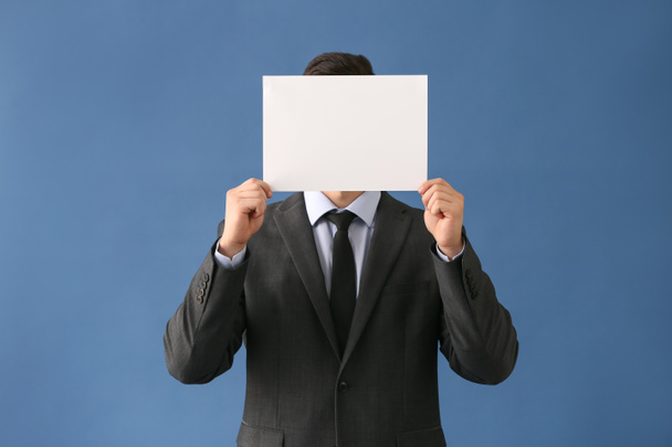Businessman hiding face behind blank sheet of paper on color background - 写真・画像