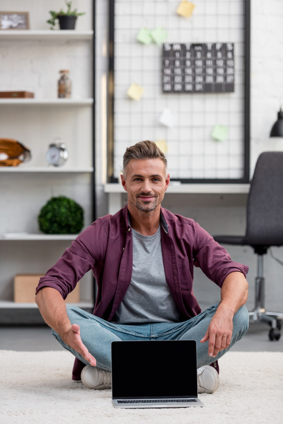 hombre guapo sentado en la oficina en casa con el ordenador portátil y apuntando a la pantalla en blanco
 - Foto, Imagen