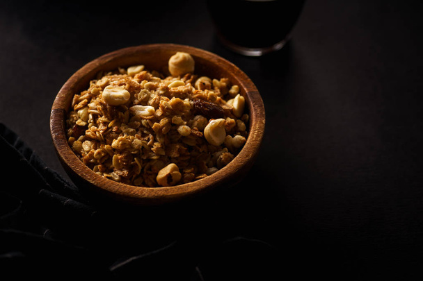 Roasted granola with nuts in wooden bowl with cup of coffee on black table  - Fotoğraf, Görsel