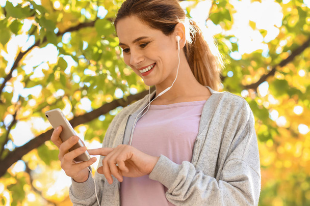 Urheilullinen nainen kuuntelemassa musiikkia syksyllä puistossa
 - Valokuva, kuva