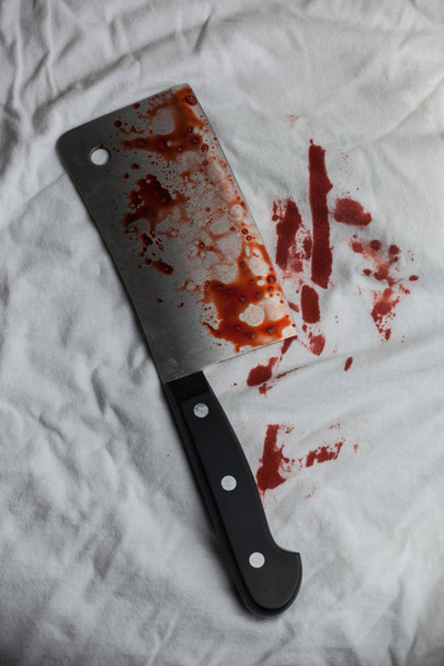 A bloody meat cleaver sits on a white t-shirt. - Foto, afbeelding