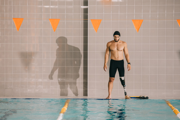 muscular young sportsman with artificial leg looking at indoor swimming pool - Foto, immagini
