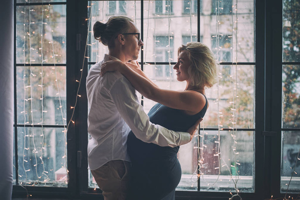 Man and pregnant woman dance near window in loft style room - 写真・画像