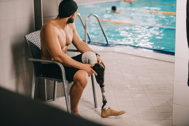 deportista atlético con pierna artificial sentado en la silla en la piscina cubierta
 - Foto, Imagen