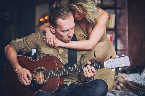 man playing a guitar and his pregnant wife are sitting on a bed in a loft room - 写真・画像