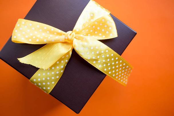Brown gift box with yellow ribbon on orange background. copy space. - Fotó, kép