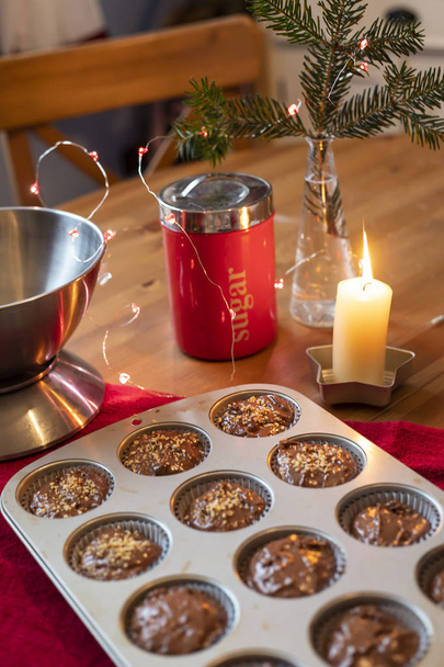 Table composition with chocolate muffins in metal tin, candle and tools. Table is festive, with a pine branch in a vase and stringlights. - Photo, Image