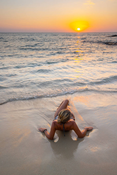 Beautiful young woman on a sandy ocean beach in a swimsuit at sunset - Foto, imagen