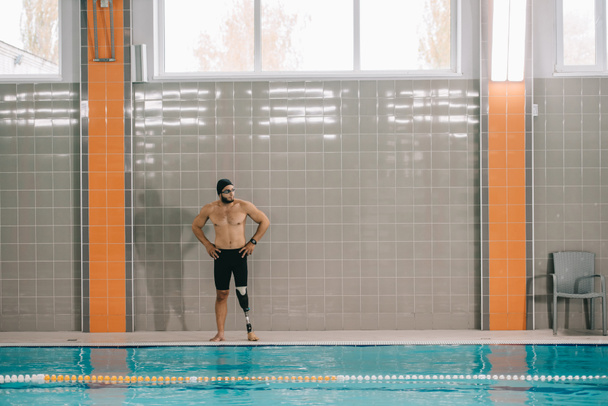 atletische jonge sporter met kunstmatige been staande op zwembad op overdekt zwembad - Foto, afbeelding