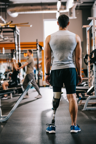 rear view of sportsman with artificial leg standing at gym - Fotó, kép