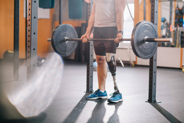 cropped shot of sportsman with artificial leg working out with barbell at gym - 写真・画像