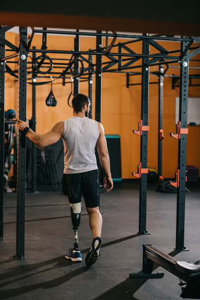 όμορφος νεαρός αθλητής με τεχνητό πόδι του ακουμπά στη Σκάλα γυμναστική στο γυμναστήριο - Φωτογραφία, εικόνα