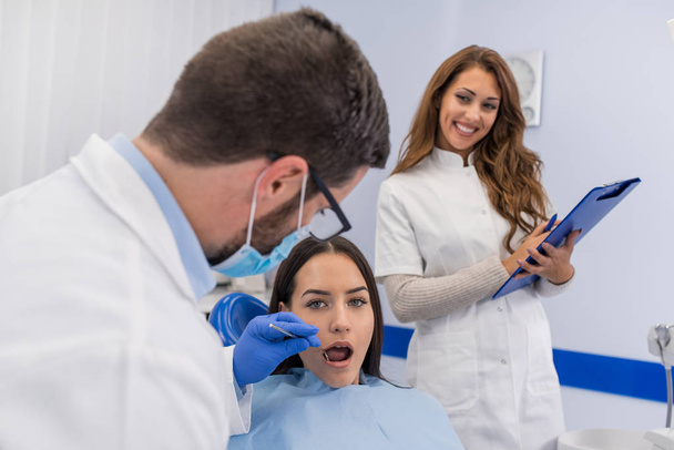 Jonge vertrouwen mannelijke tandarts medische behandeling aan een vrouwelijke patiënt bij de kliniek. Tandheelkundige kliniek concept - Foto, afbeelding