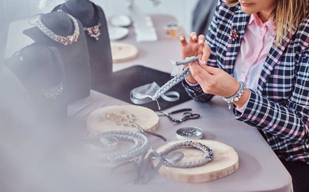 Mujer elegantemente vestida hace collares hechos a mano, trabajando con agujas e hilo en el taller
. - Foto, Imagen