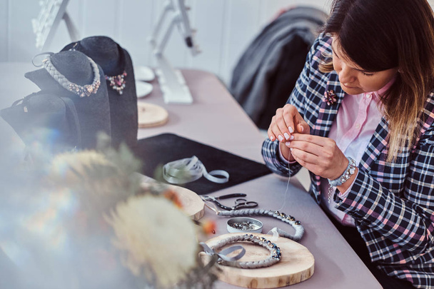 エレガントな服を着た女性、手作りネックレス、針と糸のワーク ショップで作業. - 写真・画像