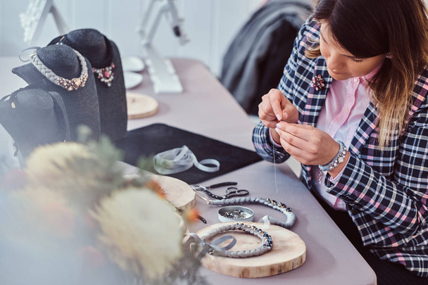 Mujer elegantemente vestida hace collares hechos a mano, trabajando con agujas e hilo en el taller
. - Foto, imagen