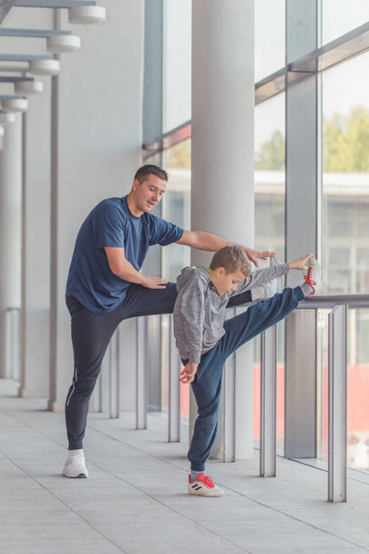 Little boy and his trainer doing stretching legs exercises together at a sports center. Father and son spend time together and lead a healthy lifestyle.Working Out Together. Fitness Day.  - Foto, imagen