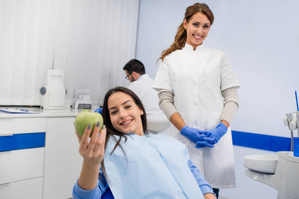 Girl patient in dental chair smiling with green apple - Valokuva, kuva